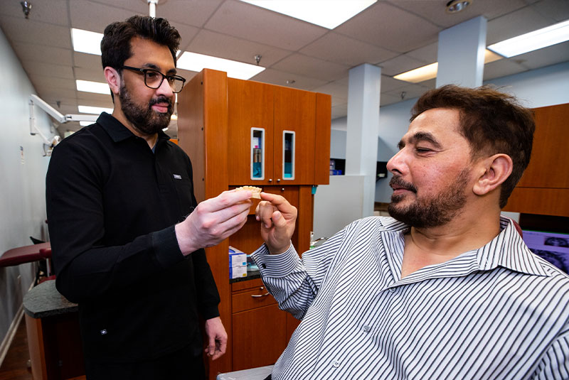 Dr. Asim showing dental patient a model of full arch dental implants